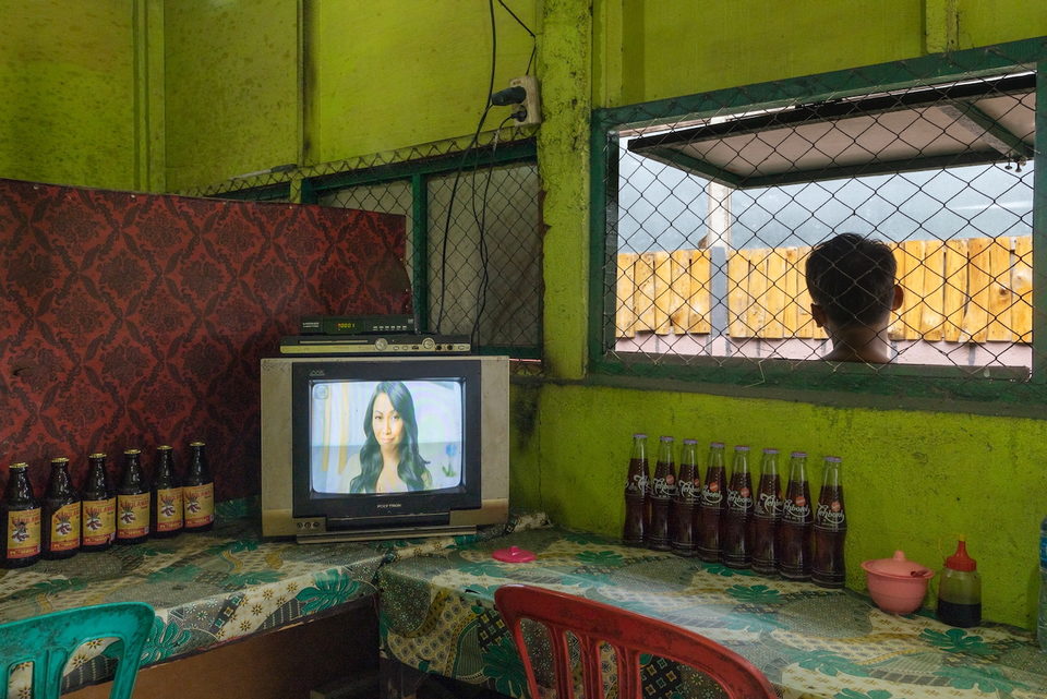 A television on a counter beside a barred window and rows of bottles.