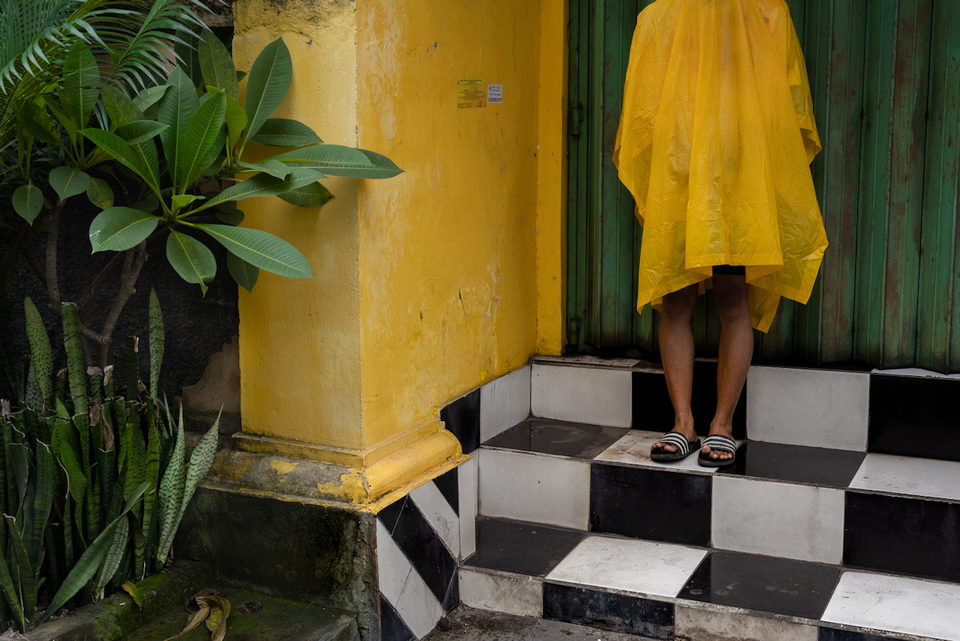 A yellow raincoat hangs in a doorway above black and white tiles.