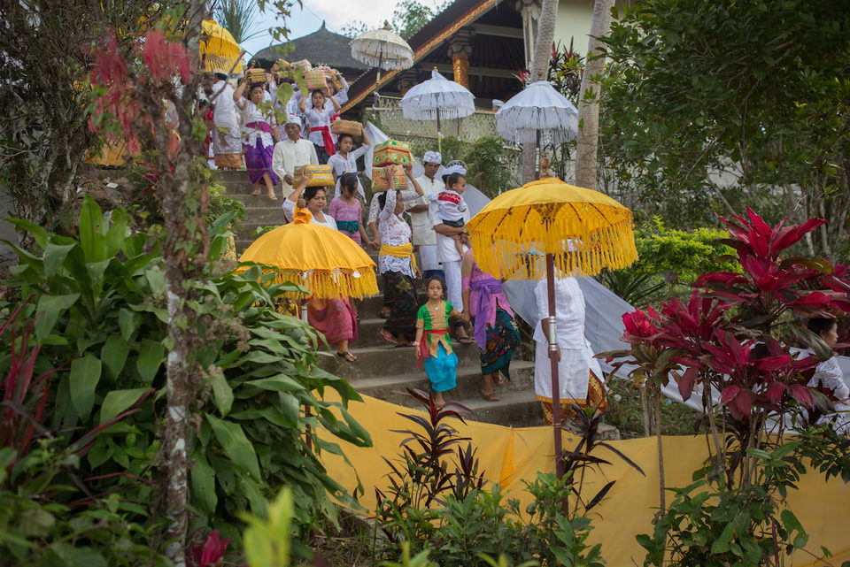 A procession under yellow and white ceremonial umbrellas descends temple steps.