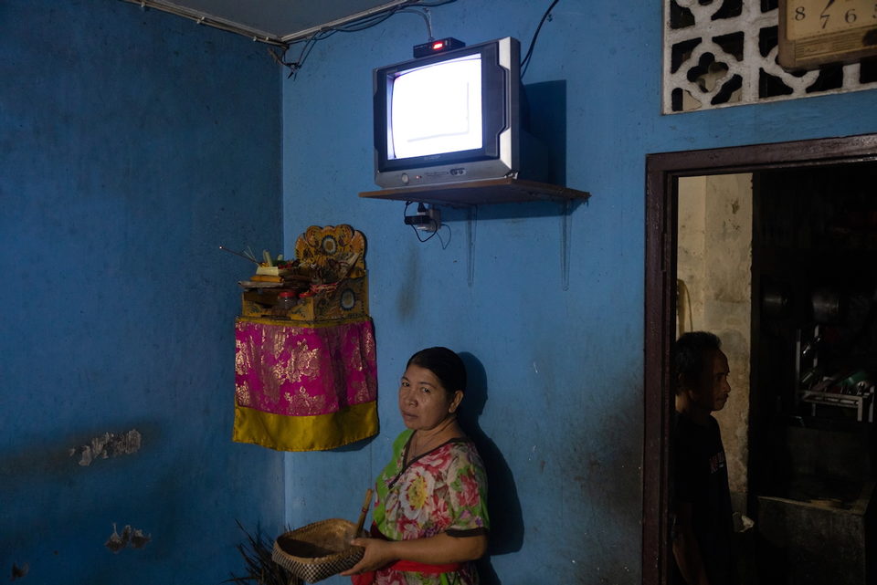 A woman stands beneath a wall-mounted television beside a shrine.