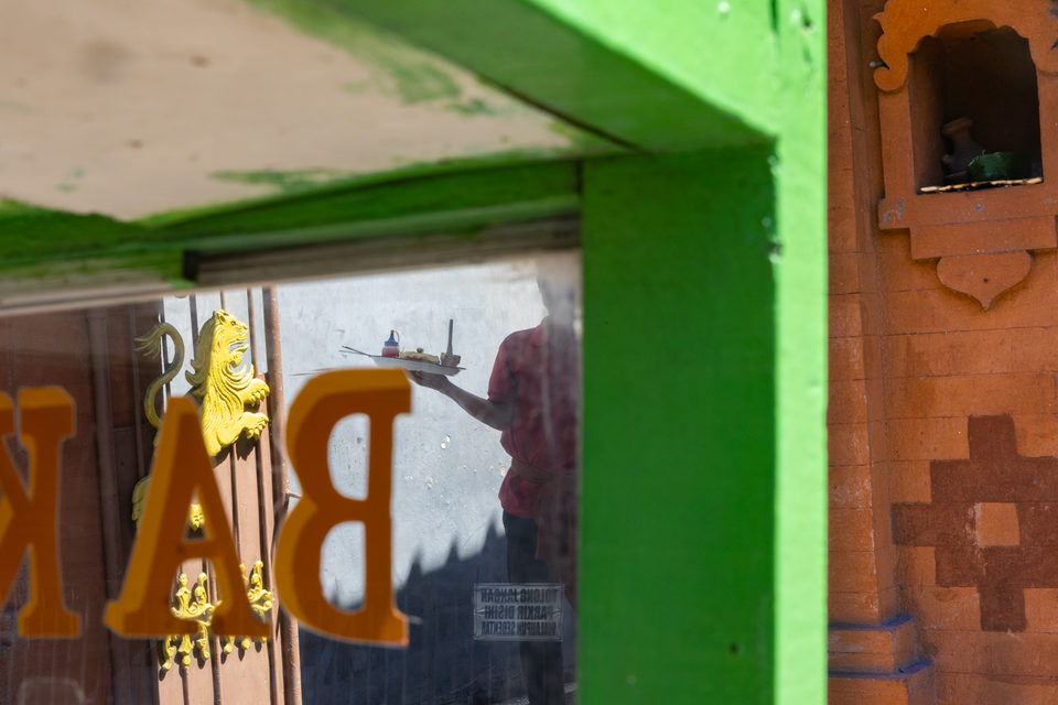 Gold lettering on green framing, a figure carrying a tray reflected in the glass.