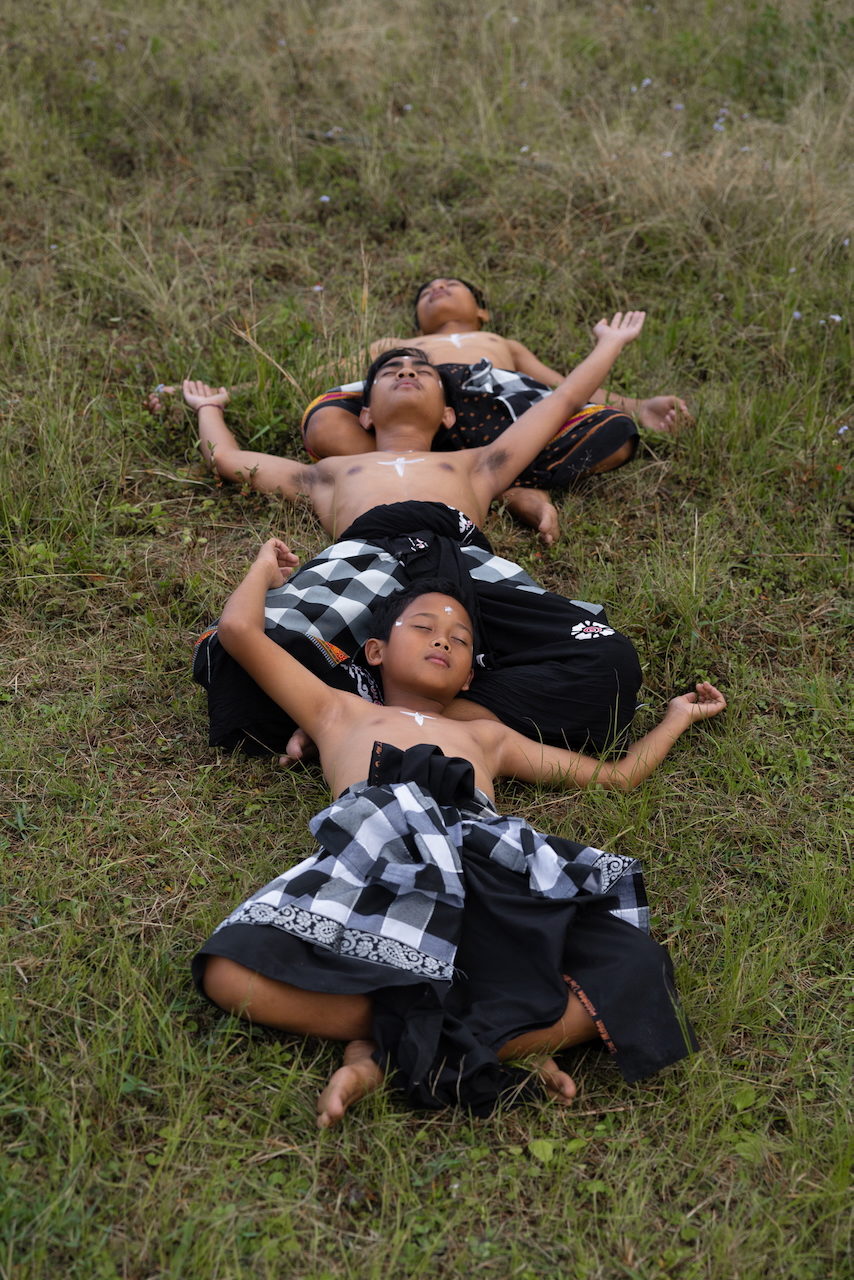 Young people lie on grass in checked ceremonial cloth.