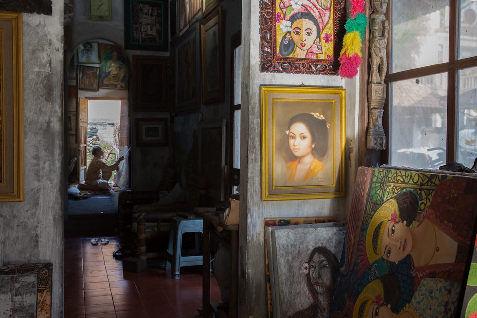A room hung with painted portraits, a framed painting of a woman in the foreground.