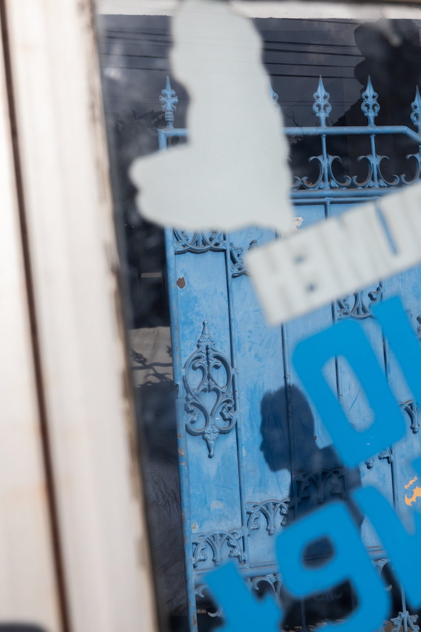 Blue shopfront grillework seen through pale lettering on the glass.