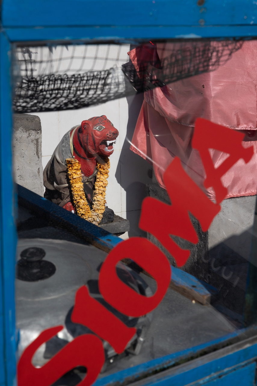 A red temple guardian statue in a marigold garland behind red lettering.