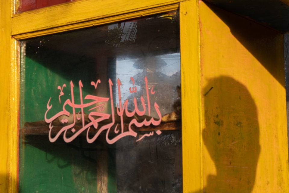 Pink Arabic calligraphy on a yellow-framed cart window.