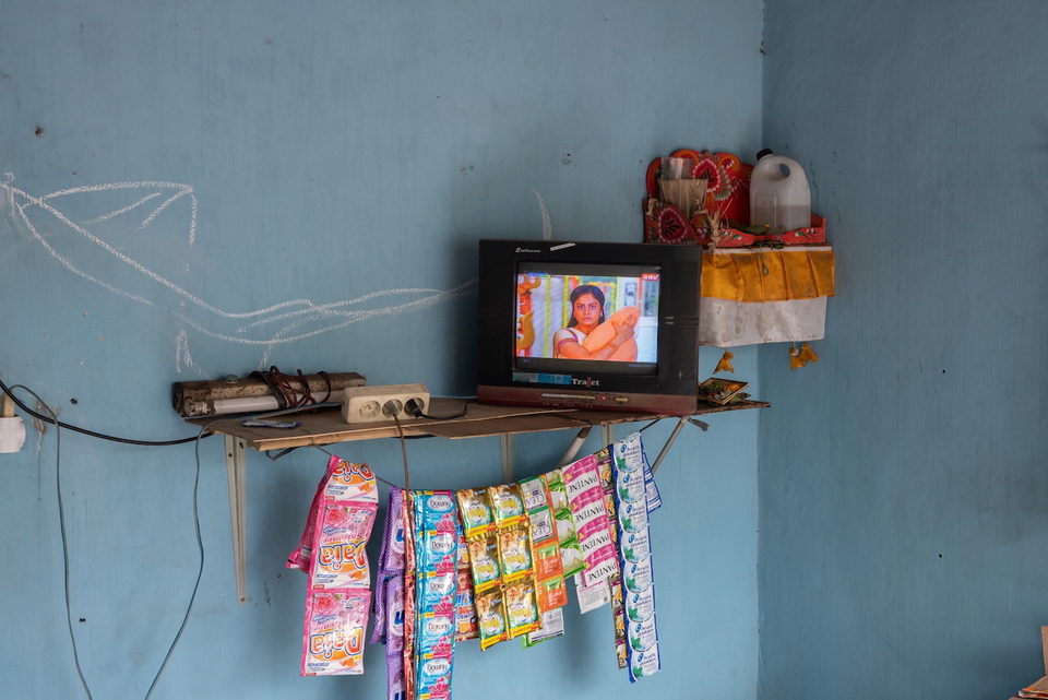 A television on a wall bracket above rows of hanging sachets.