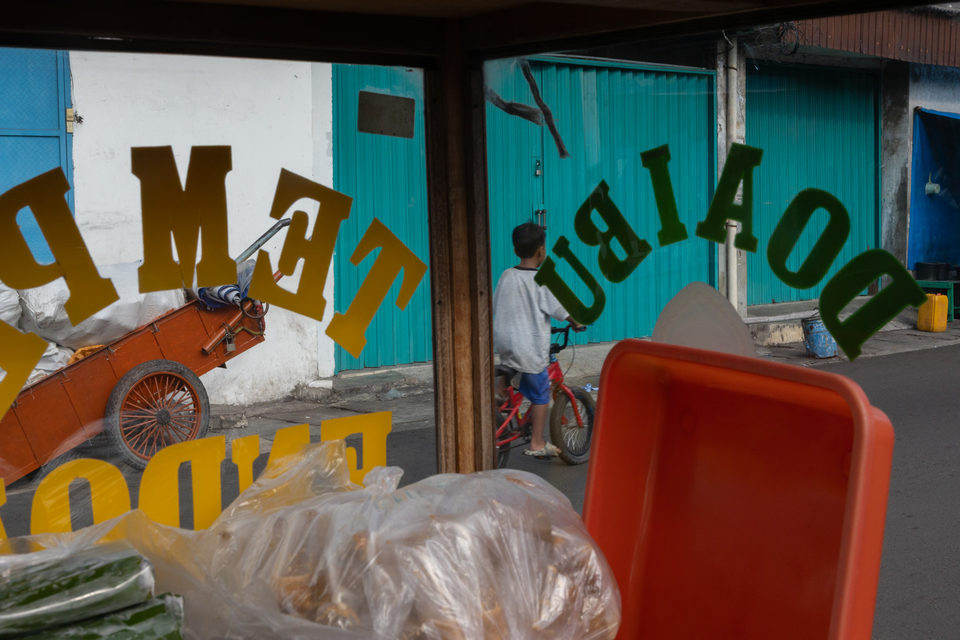 Yellow letters on green glass, a child on a bicycle by a turquoise wall.