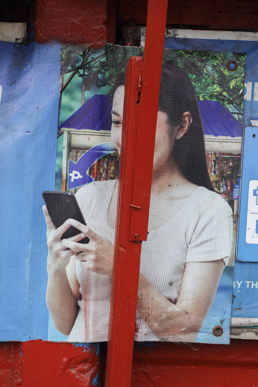 A billboard of a woman looking at her phone, split by a red pillar.