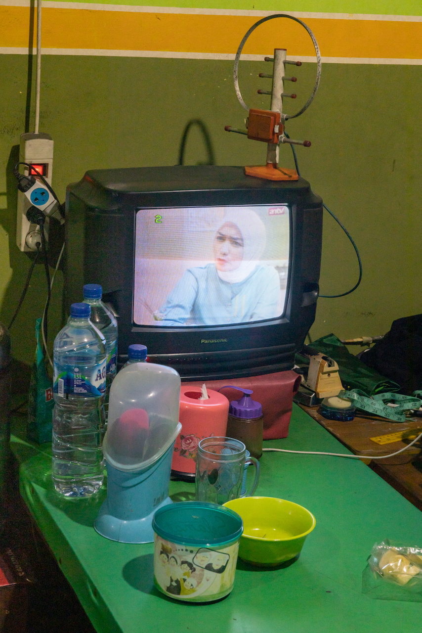 A television on a green table among bottles and jars.