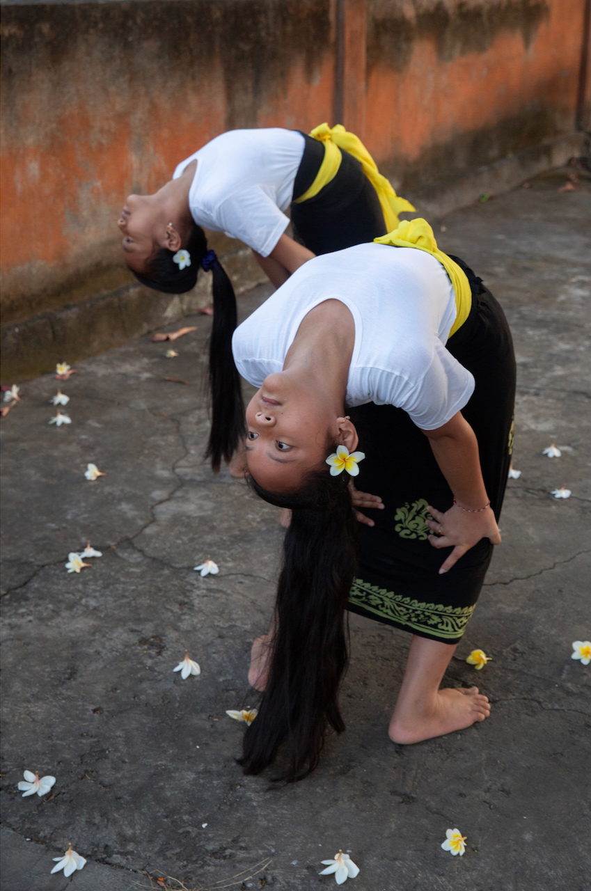 A girl bends backwards in a dance pose on flower-strewn ground.