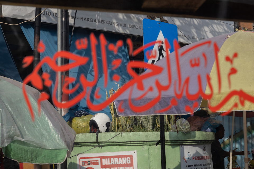Red Arabic calligraphy on the glass above a green stall and street signs.