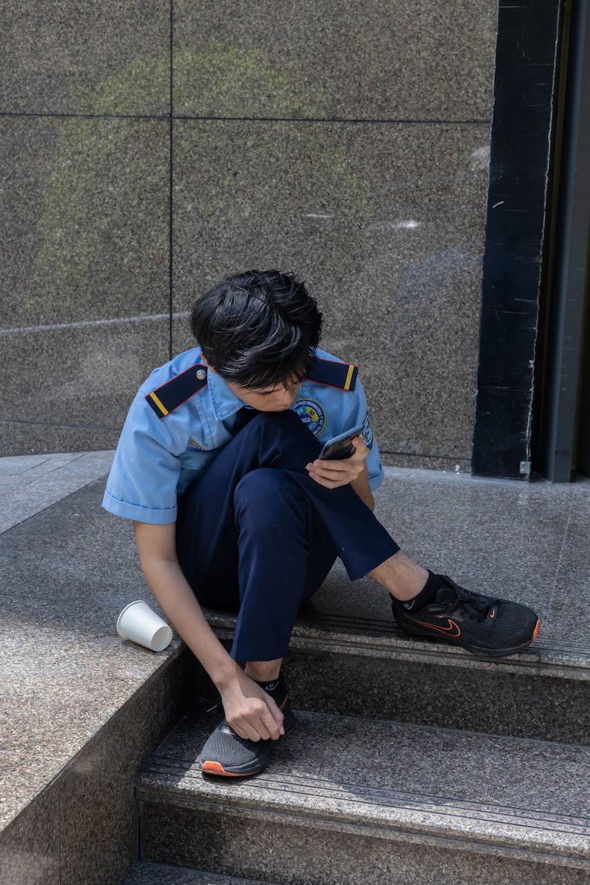 A young officer in blue uniform sits on steps looking at a phone.