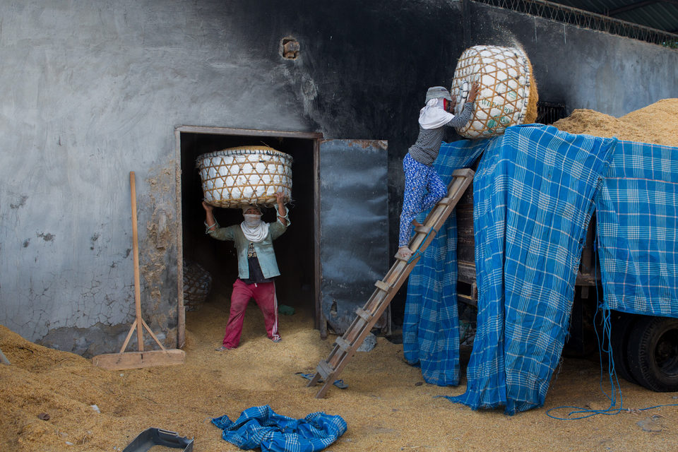 A child carries a woven basket on their head in a doorway hung with blue checked cloth.