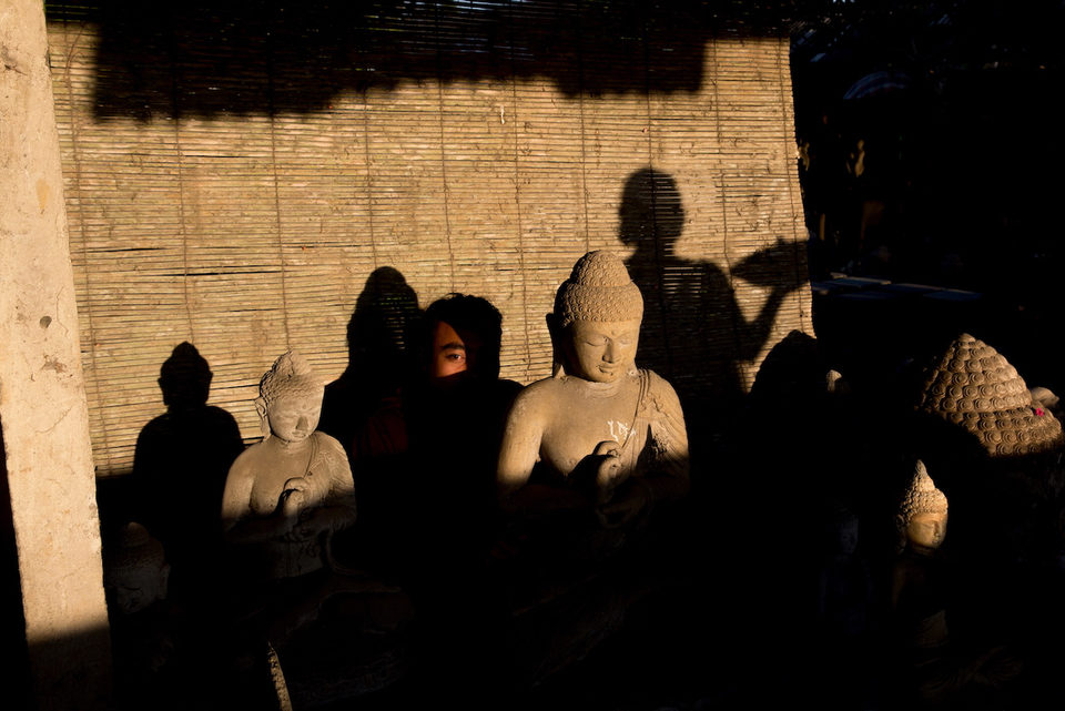 Stone Buddha figures in shadow against a woven bamboo blind lit by low sun.